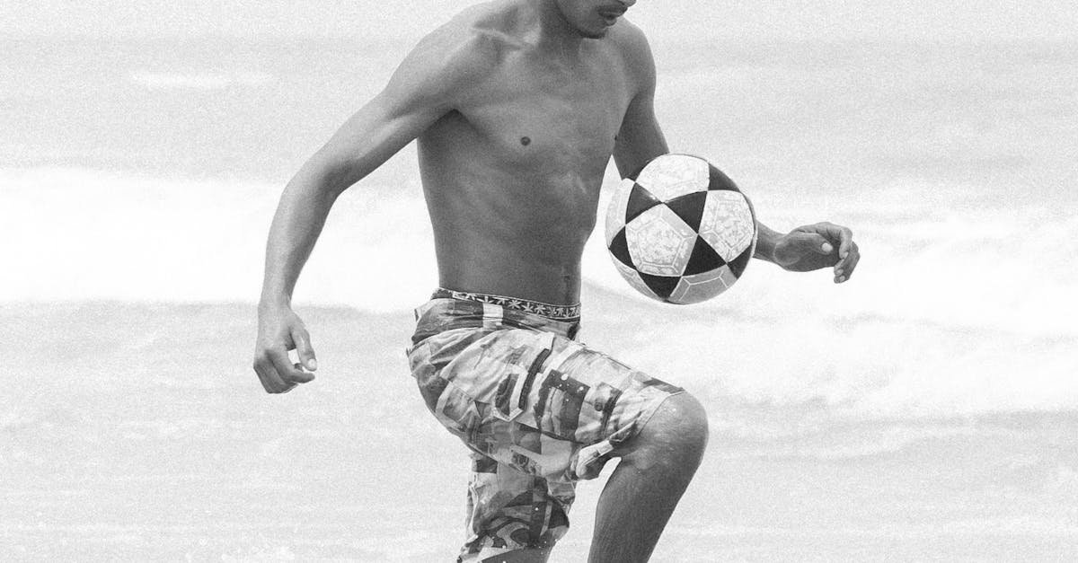 Black and white photo of a young man skillfully playing soccer on the beach.